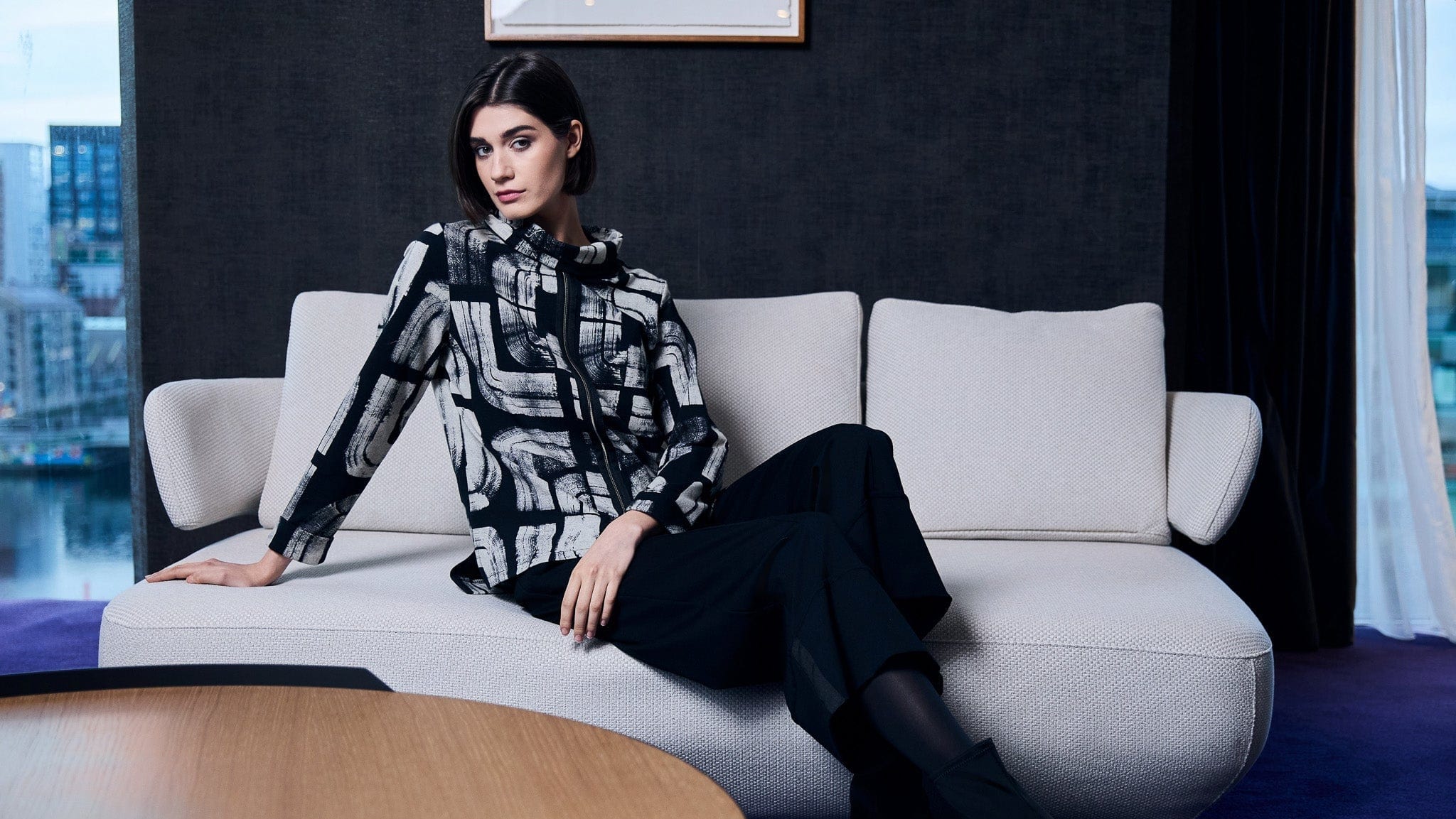 Woman sitting on a modern sofa in an elegant room with cityscape view
